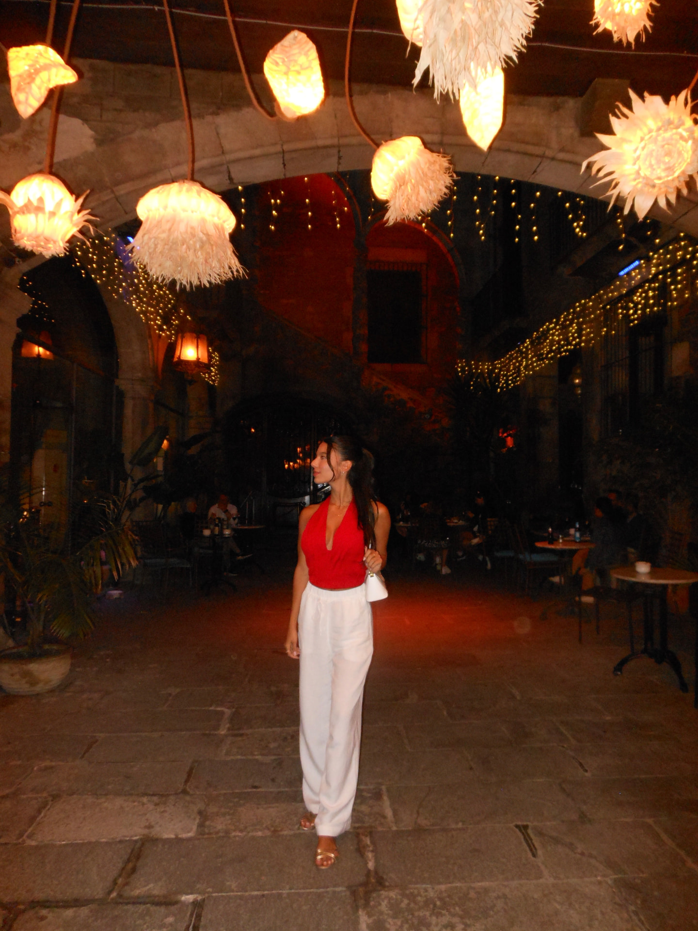 Red halter top with white wide-leg trousers under lantern-lit courtyard